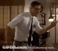 Man In White Shirt And Tie Standing In Living Room With Lamp GIF