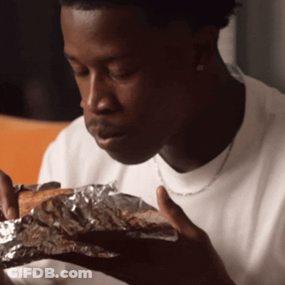 Man In White Shirt Eating Bread Wrapped In Tin Foil GIF