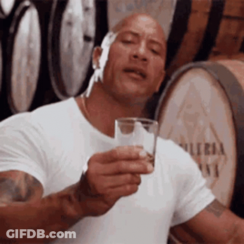 Man In White Shirt Holding Glass Of Water In Front Of Barrels GIF