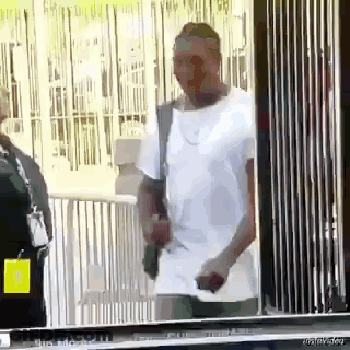 Man In White Shirt Holding Gun In Front Of Fence GIF