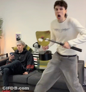 Man In White Shirt Holding Stick In Front Of Couch GIF
