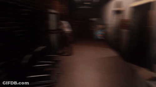 Man In White Shirt In Dark Hallway With Elevator Sign GIF