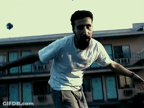 Man In White Shirt In Front Of Building With Blue Doors GIF
