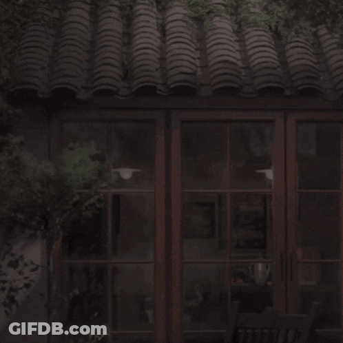 Man In White Shirt In Front Of Building With Tiled Roof GIF