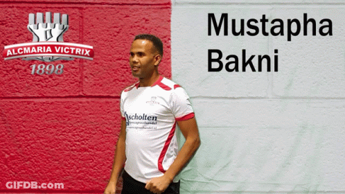 Man In White Shirt In Front Of Mustapha Bakni Wall GIF