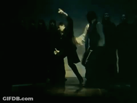 Man In White Shirt In Front Of People In Black Hoods GIF