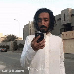 Man In White Shirt Looking At Phone With Hemoji.net GIF