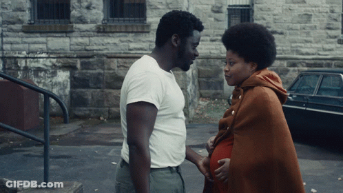 Man In White Shirt Next To Pregnant Woman In Brown Blanket GIF