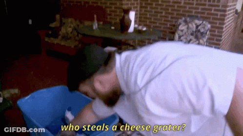 Man In White Shirt Reaching Into Blue Bin Asking Who Steals Cheese Grater GIF