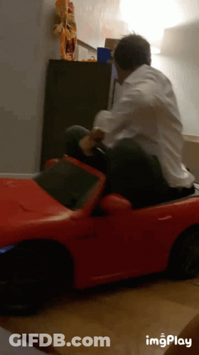 Man In White Shirt Riding Red Toy Car GIF
