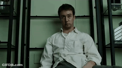 Man In White Shirt Sitting At Bookshelf GIF