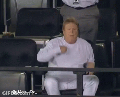 Man In White Shirt Sitting In Stadium With Fist In Air GIF