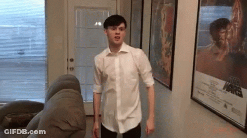 Man In White Shirt Standing Next To Couch And Star Wars Poster GIF