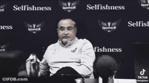 Man In White Shirt Surrounded By Selfishness Words GIF