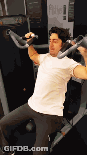 Man In White Shirt Using Gym Machine With Sign Saying Fitness GIF
