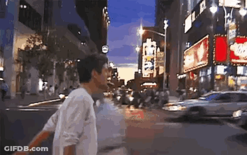 Man In White Shirt Walking Down Busy City Street At Night GIF