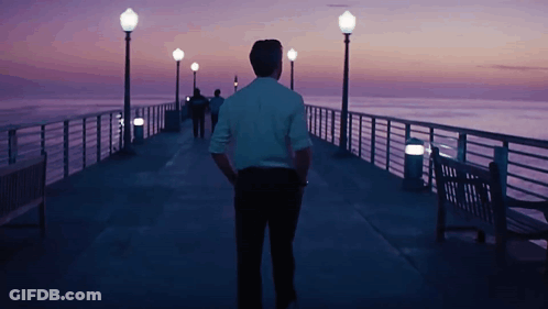 Man In White Shirt Walking Down Pier At Night GIF