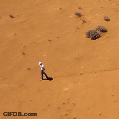 Man In White Shirt Walking In Sandy Desert GIF