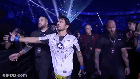 Man In White Shirt Walking Through Crowd In Dark Room GIF