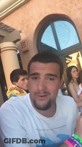 Man In White Shirt With Wave In Front Of Building GIF