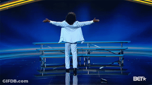 Man In White Suit Arms Outstretched On Stage With BET Logo GIF