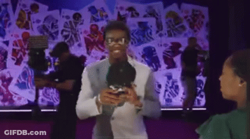 Man In White Suit Holding Microphone Talking To Woman In Green Shirt GIF