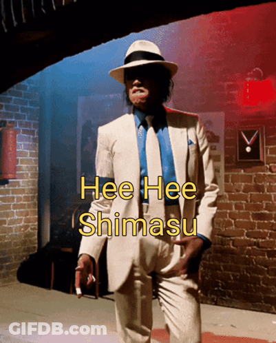 Man In White Suit In Front Of Brick Wall Saying Hee Hee Shimasu GIF
