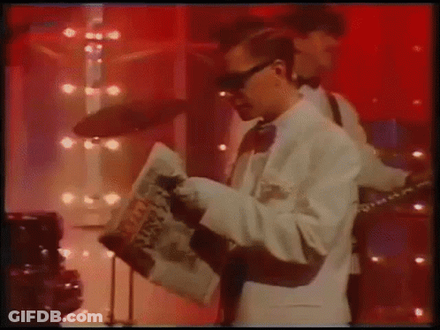 Man In White Suit Playing Guitar And Reading Newspaper GIF