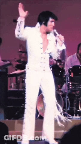 Man In White Suit Singing Into Microphone On Stage GIF