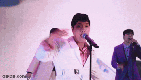 Man In White Suit Singing Into Microphone With Man In Purple Suit GIF