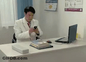 Man In White Suit Sitting At Desk Looking At Phone GIF
