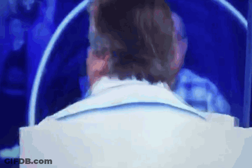 Man In White Suit Sitting In Front Of Screen GIF