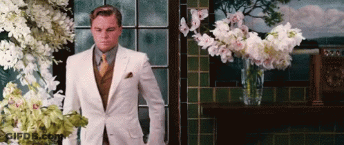 Man In White Suit Standing By Window With Flowers GIF