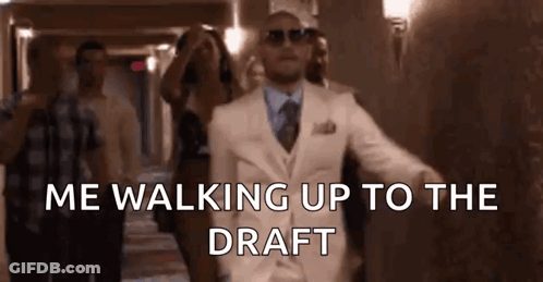 Man In White Suit Walking Up Hallway With People GIF