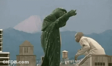 Man In White Sweater Standing Next To Giant Monster GIF