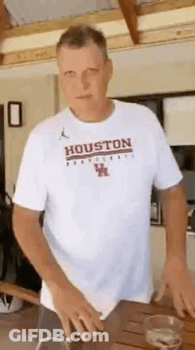 Man In White T-Shirt Saying Houston Standing At Table GIF