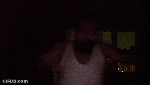 Man In White Tank Top In Front Of This Is Mustafa Sign GIF