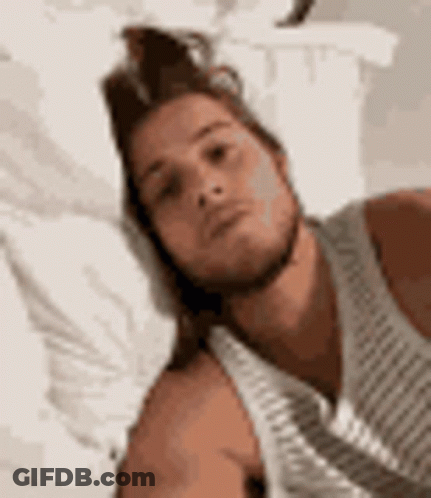 Man In White Tank Top Laying On Bed With Pillow GIF