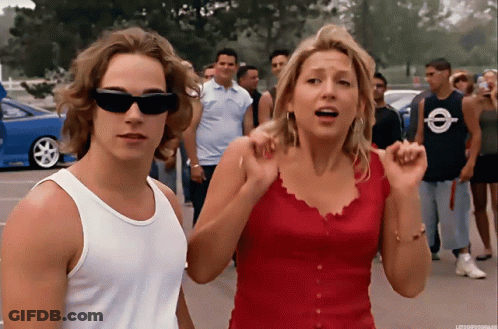 Man In White Tank Top Next To Woman In Red GIF
