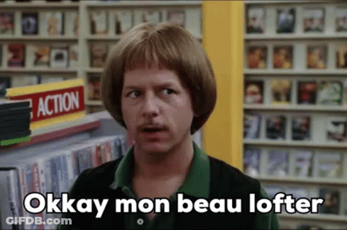 Man In Wig And Green Shirt In Front Of DVD Shelf GIF