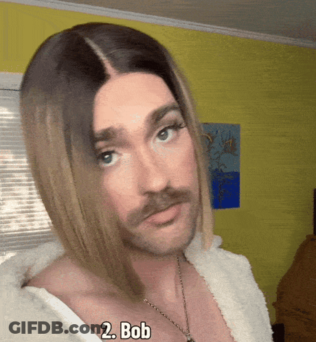 Man In Wig And Necklace With Bob On Chest GIF