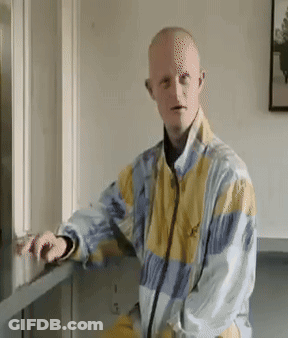 Man In Yellow And Blue Jacket Leaning Against Wall GIF