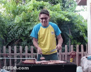 Man In Yellow And Blue Shirt Grilling Meat GIF
