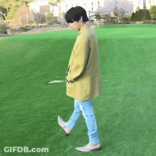 Man In Yellow Coat Walking Across Green Field GIF