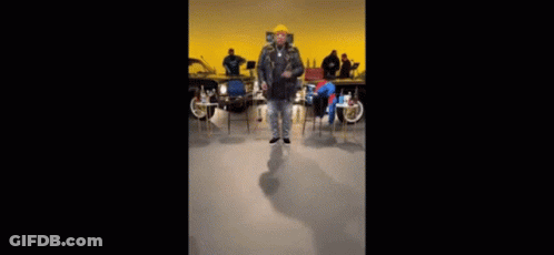 Man In Yellow Hat Dancing Among Chairs GIF