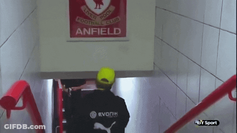 Man In Yellow Hat Walking Down Stairs In Front Of Anfield Sign GIF