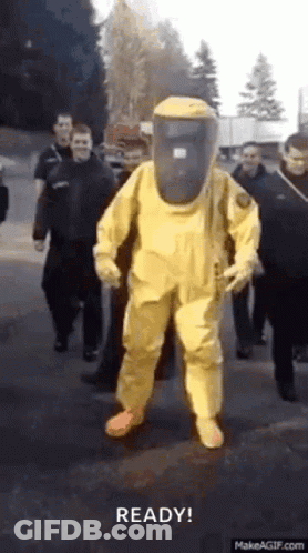 Man In Yellow Hazmat Suit Walking Street With Group GIF