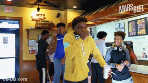 Man In Yellow Hoodie In Front Of Marsreef Sign GIF