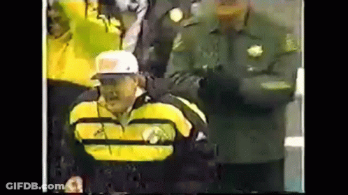 Man In Yellow Jacket And White Hat In Wheelchair In Front Of Crowd GIF
