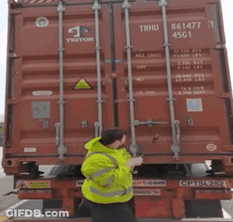 Man In Yellow Jacket Pointing At Red Triton Container GIF